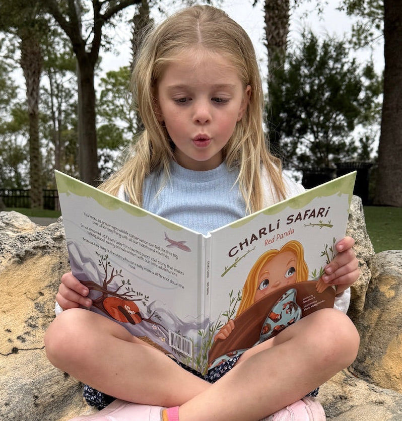 Child reading a book outdoors on a rock with trees in the background
